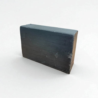Pain rectangulaire noir de savon à la nigelle et au charbon actif sur fond blanc